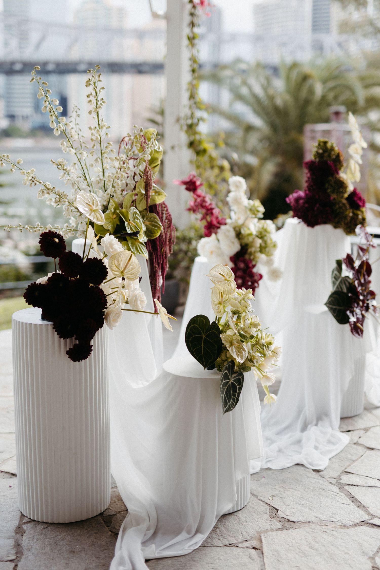 Elegant white floral arrangements in tall vases with dark and light blooms against a cityscape background.