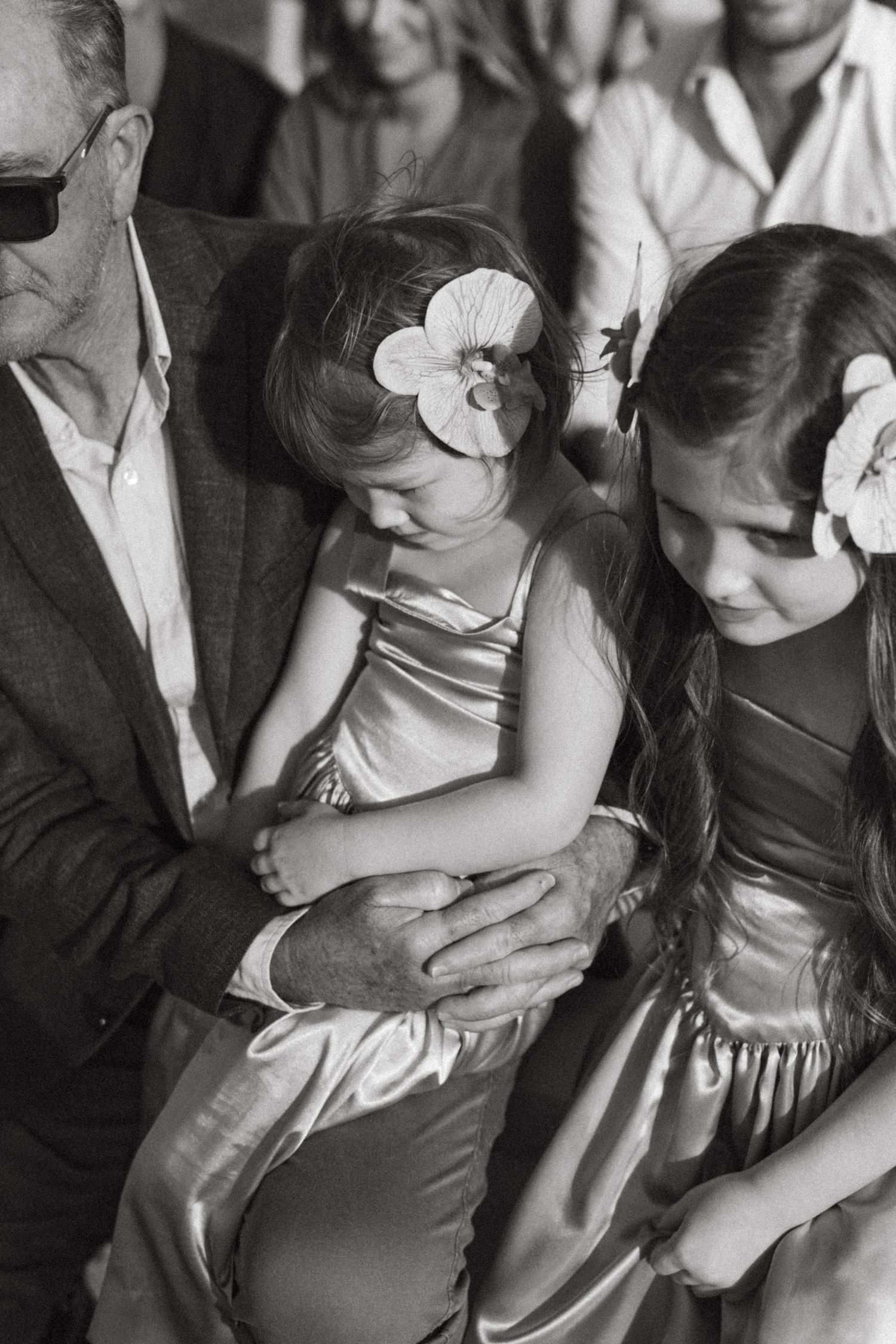 Three attendees at a formal event wearing flowers in their hair and dressed in satin dresses sit together.