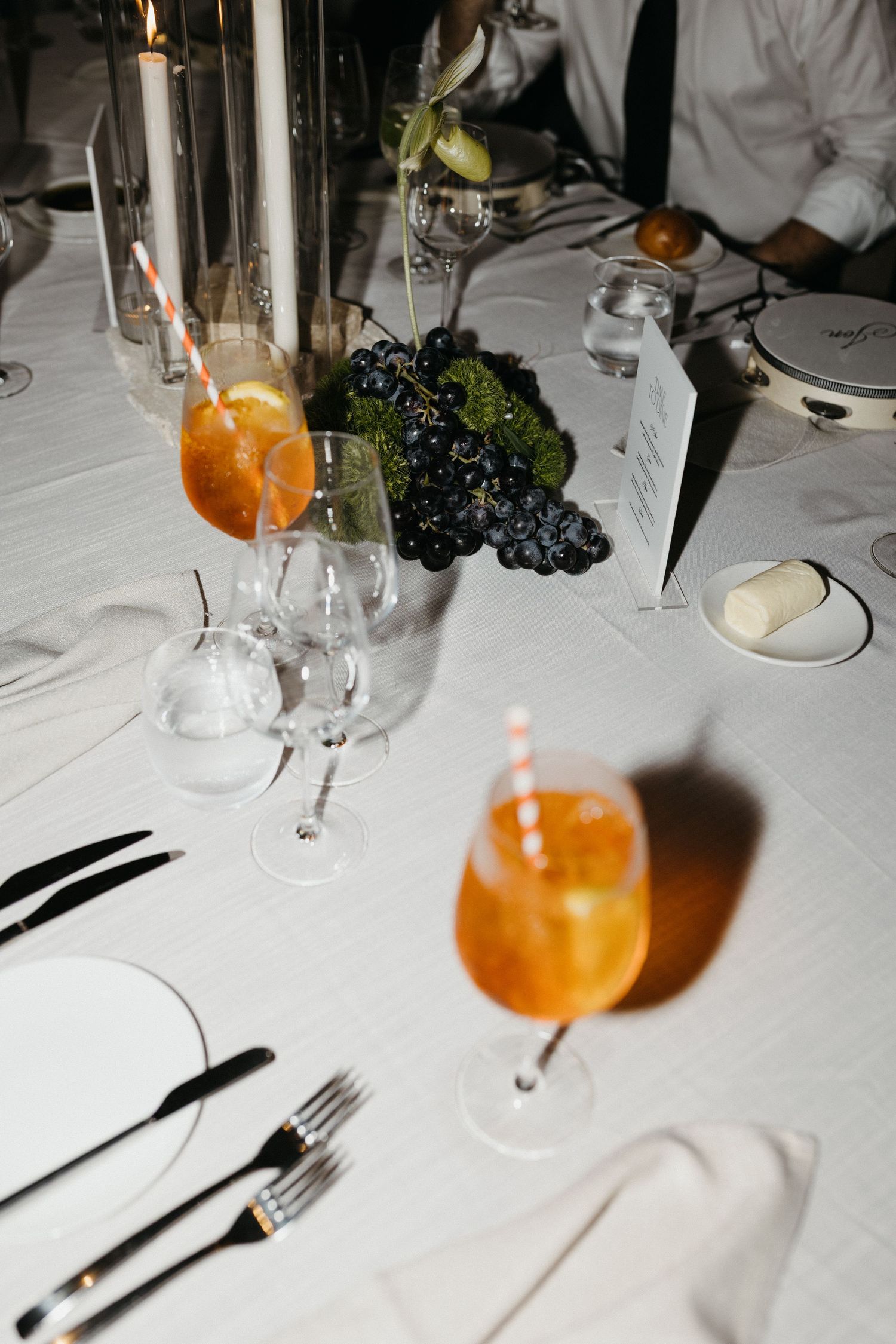 Orange cocktails and table settings with grapes sit on an elegant white tablecloth at a fine dining restaurant.