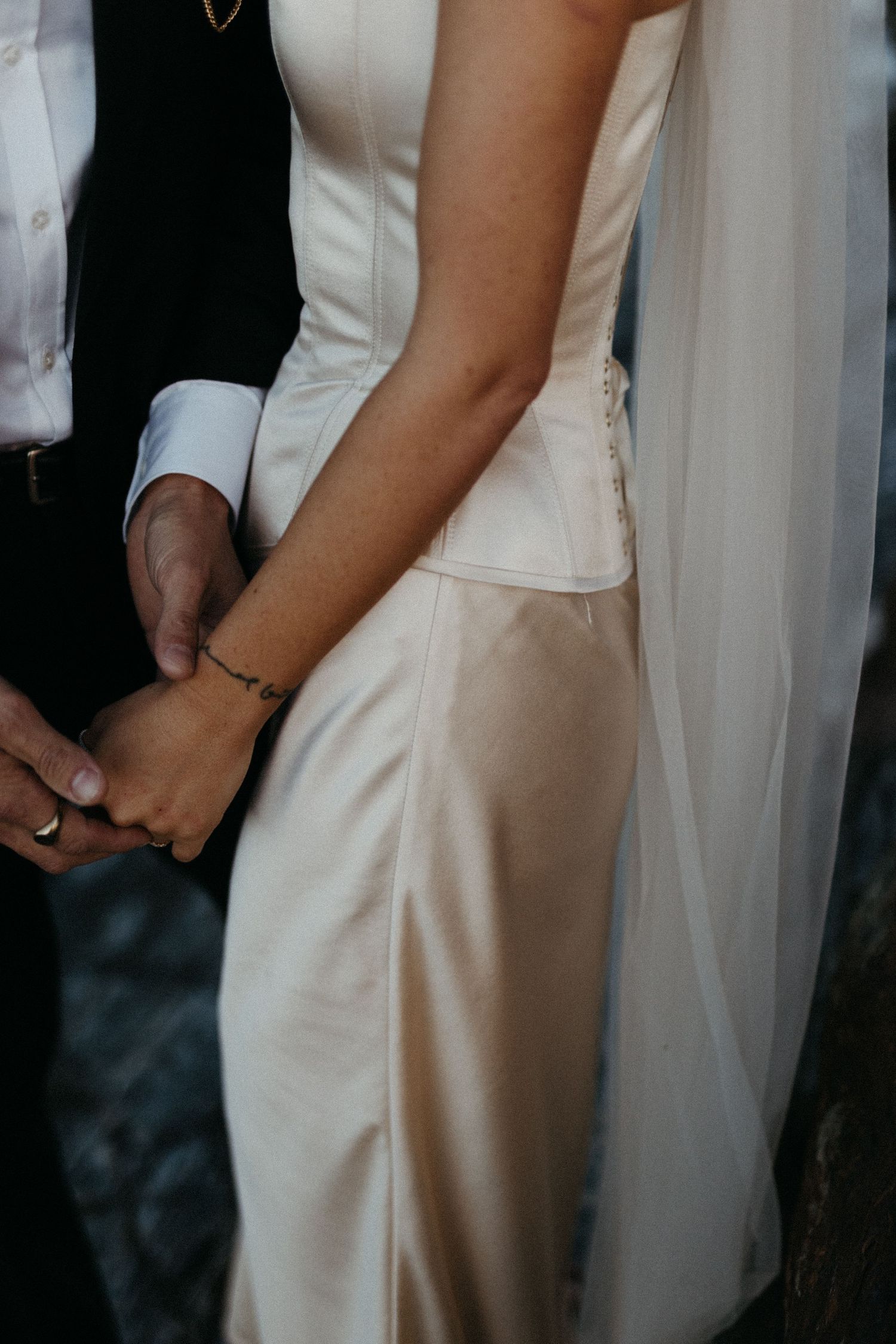 Close-up detail of couple embracing, showing white wedding dress and black suit with flowing veil.