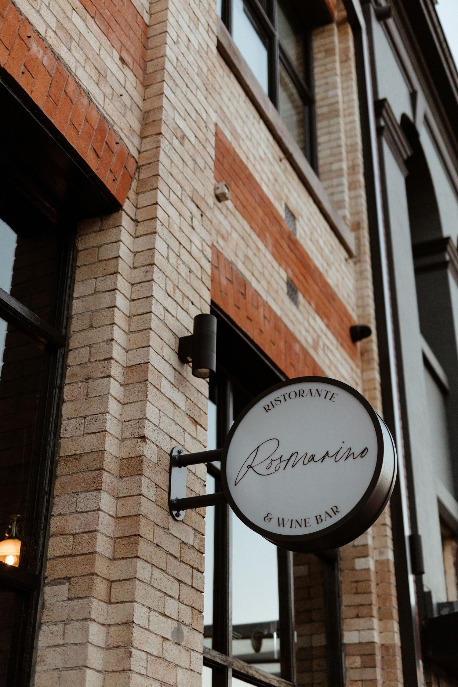 Exterior view of a restaurant and wine bar with a circular sign reading 'Botonniere' mounted on brick wall.