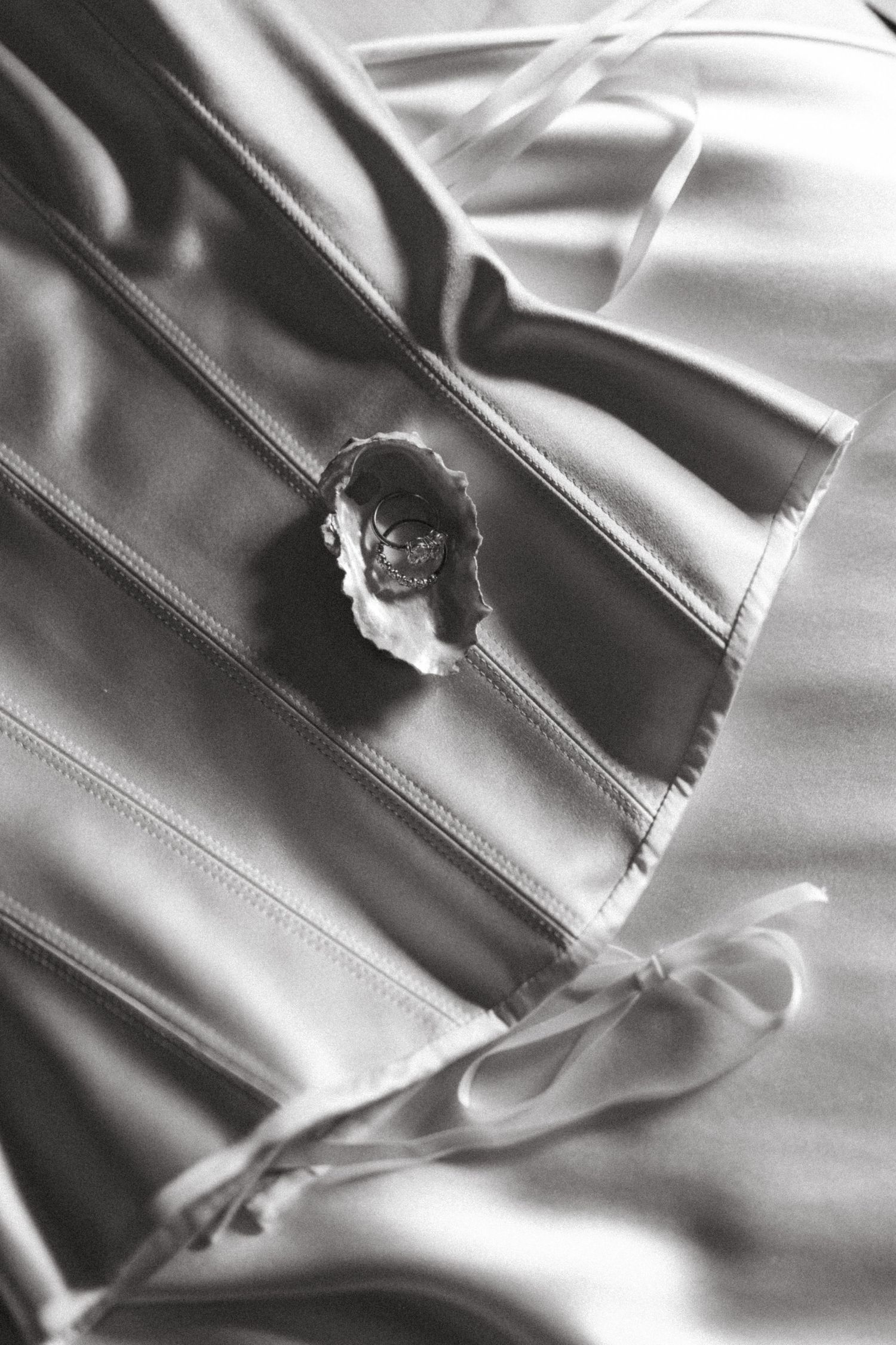 Dramatic black and white close-up of a pin or brooch casting sharp shadows on silky fabric texture.