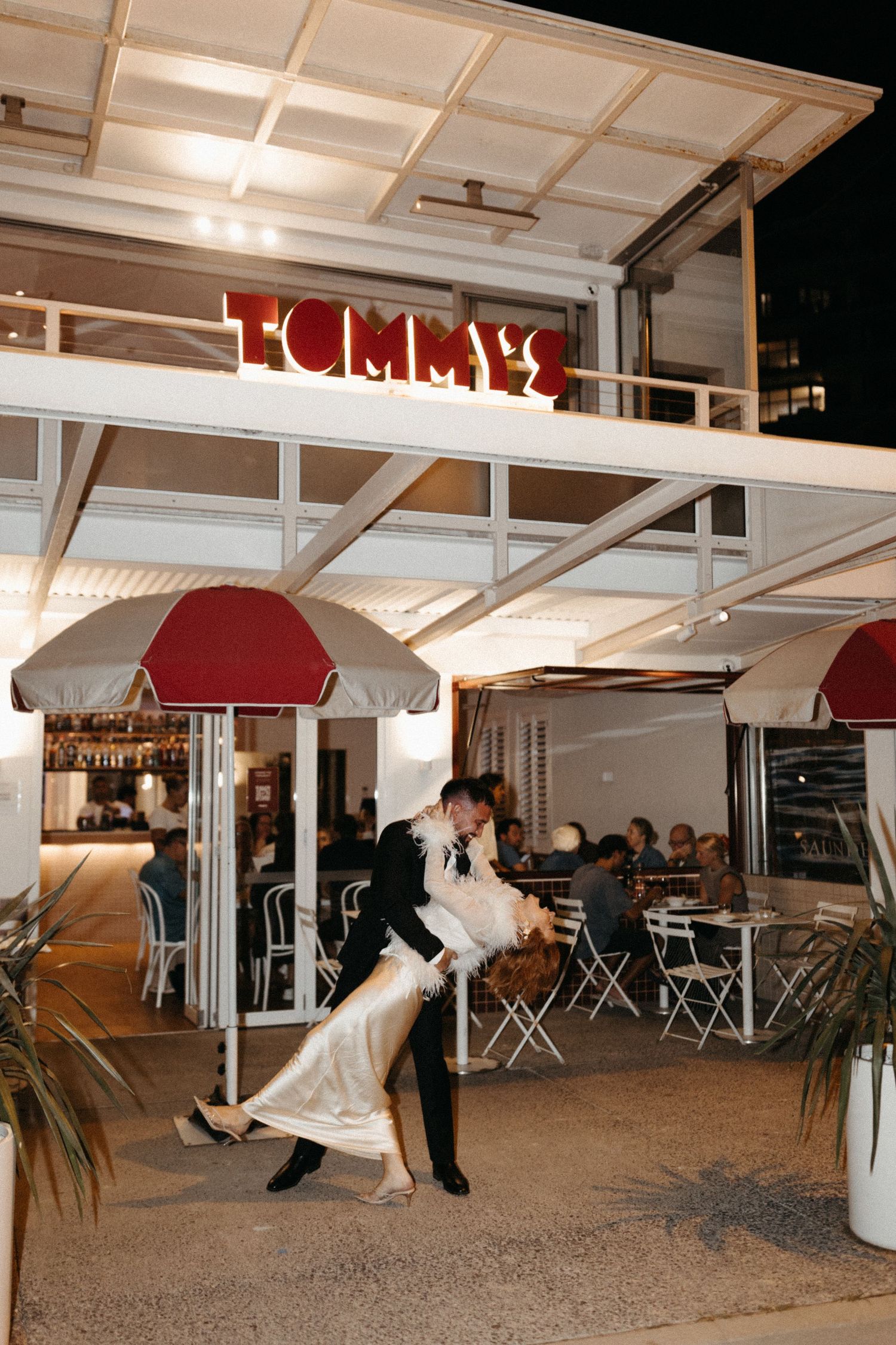 Romantic dance dip under illuminated restaurant signage at night.