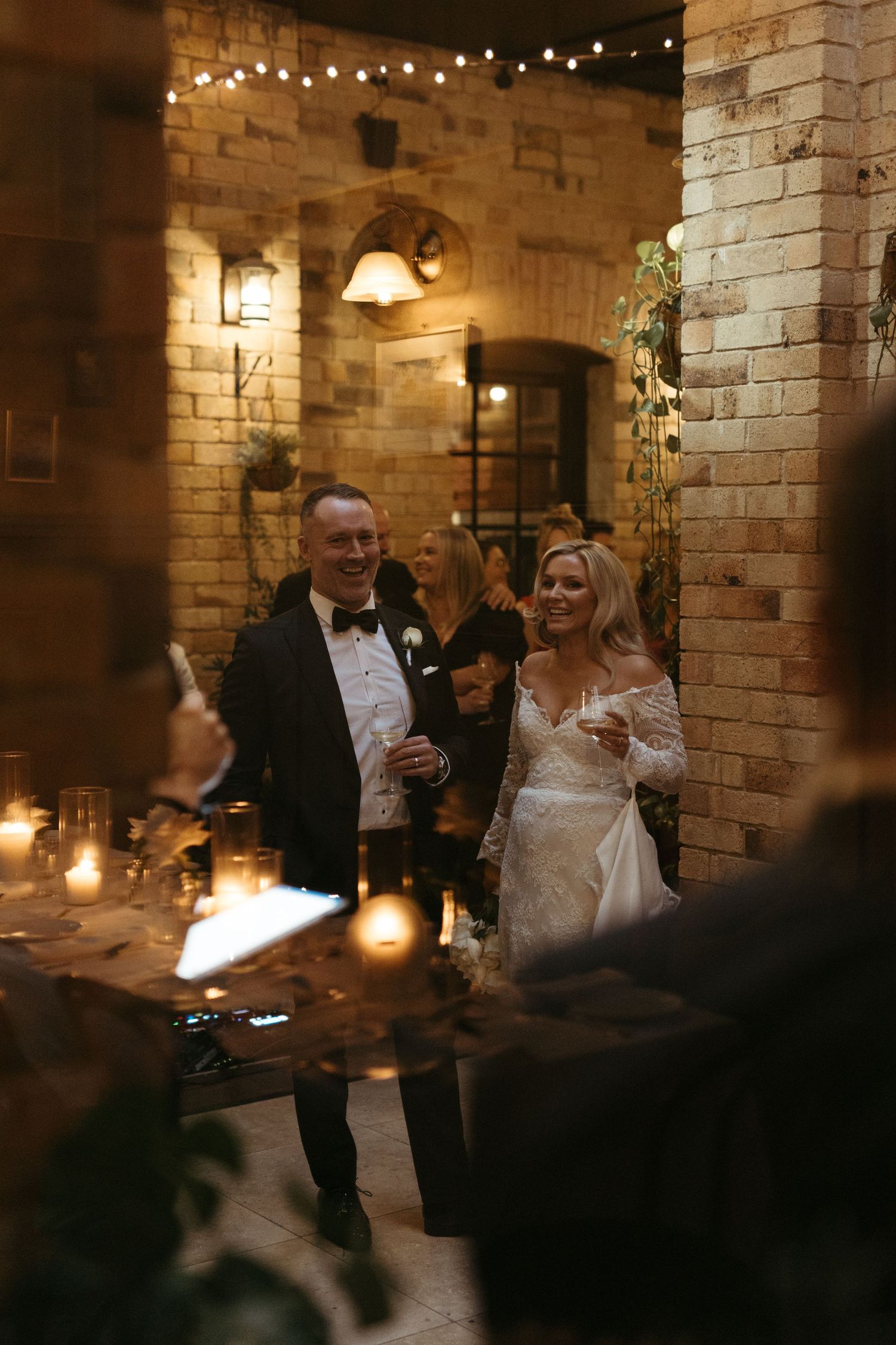 An elegant wedding reception in a rustic brick venue illuminated by string lights and candles.