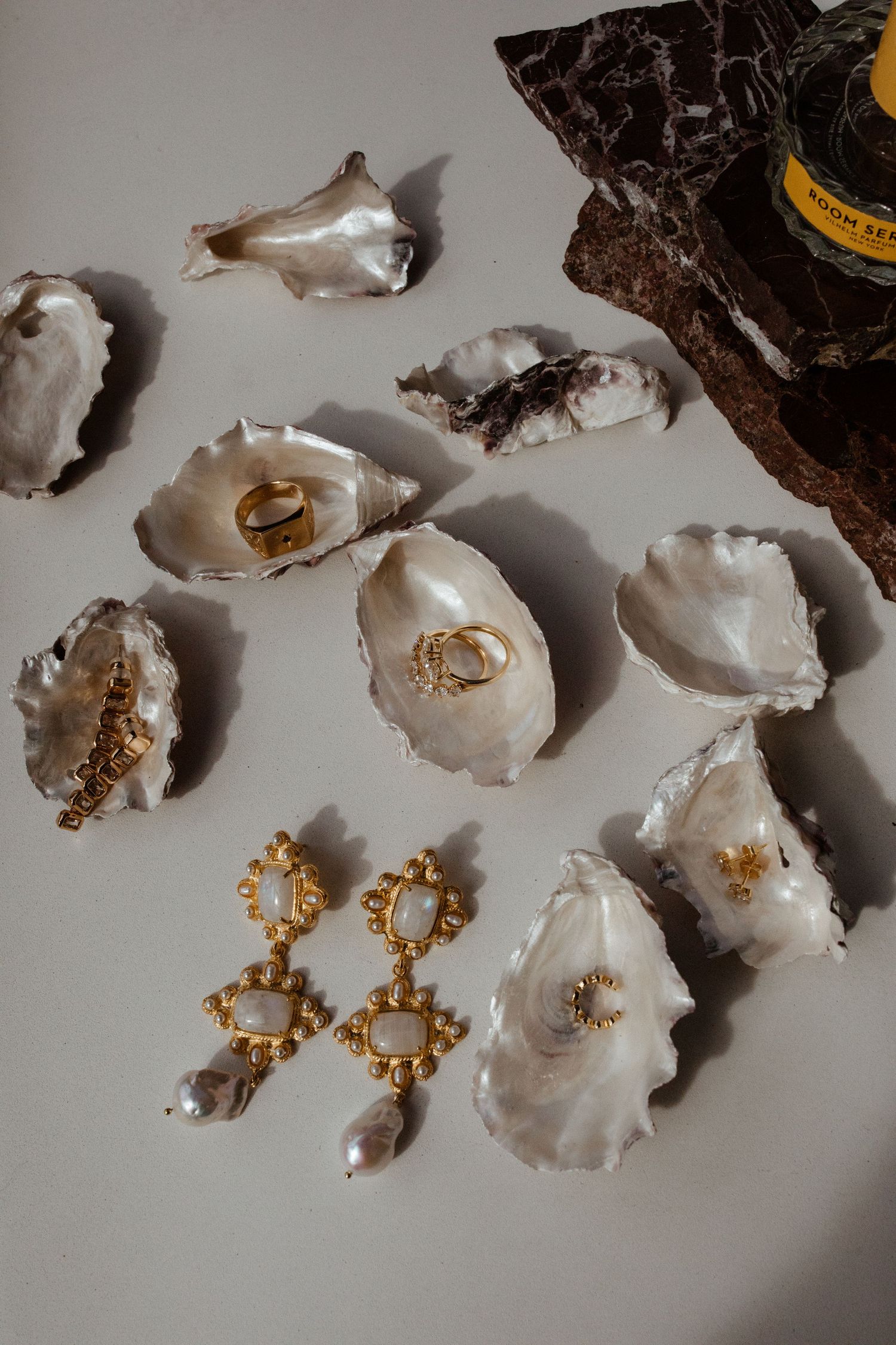 Oyster shells and ornate gold jewelry arranged on a light surface with dramatic shadows.
