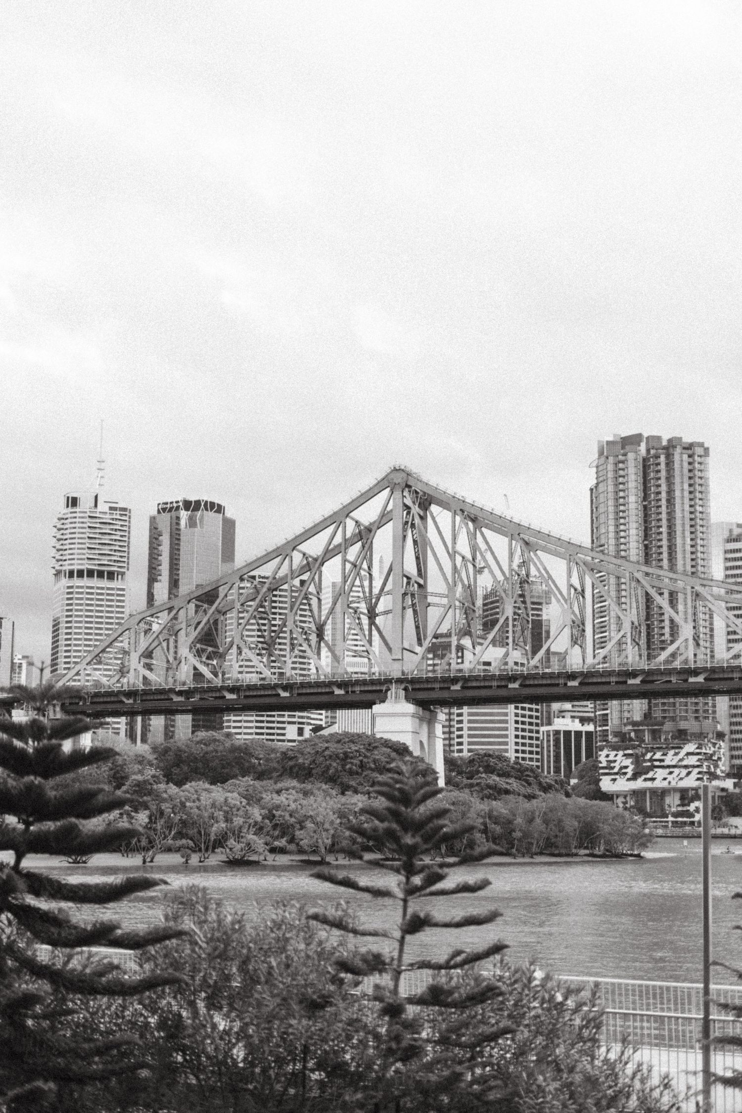 Black and white cityscape view of the Story Bridge spanning the Brisbane River with high-rise buildings in the background.