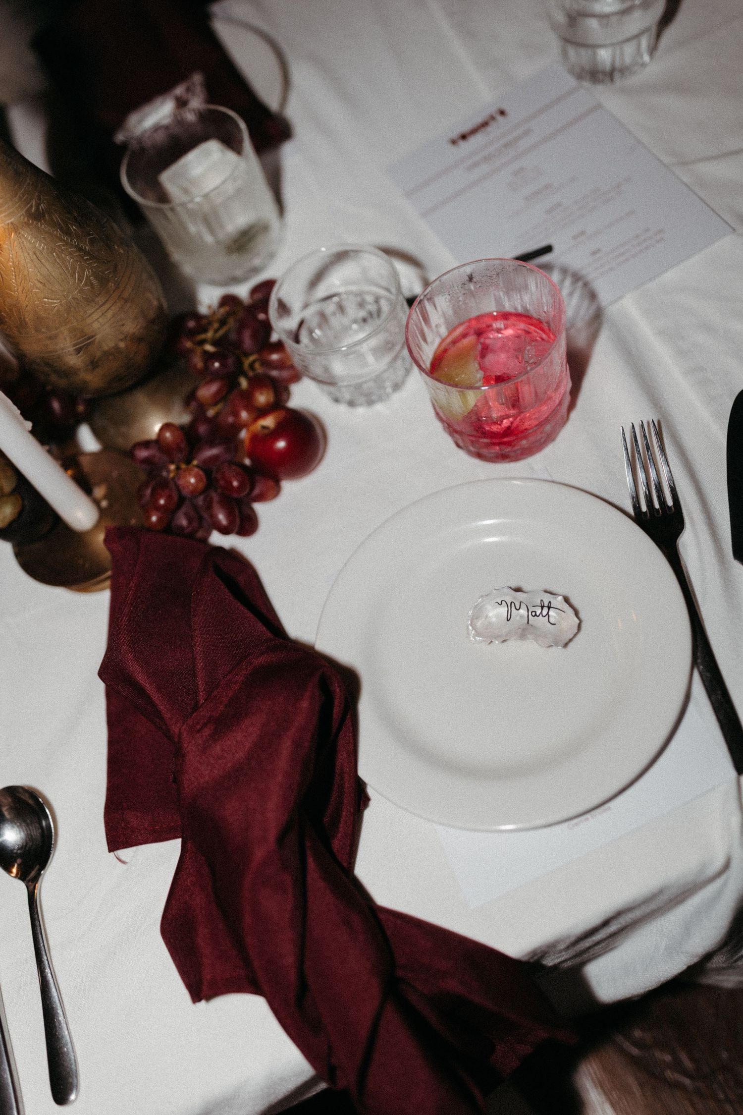 Elegant table setting with burgundy napkin, grapes, and pink cocktail.