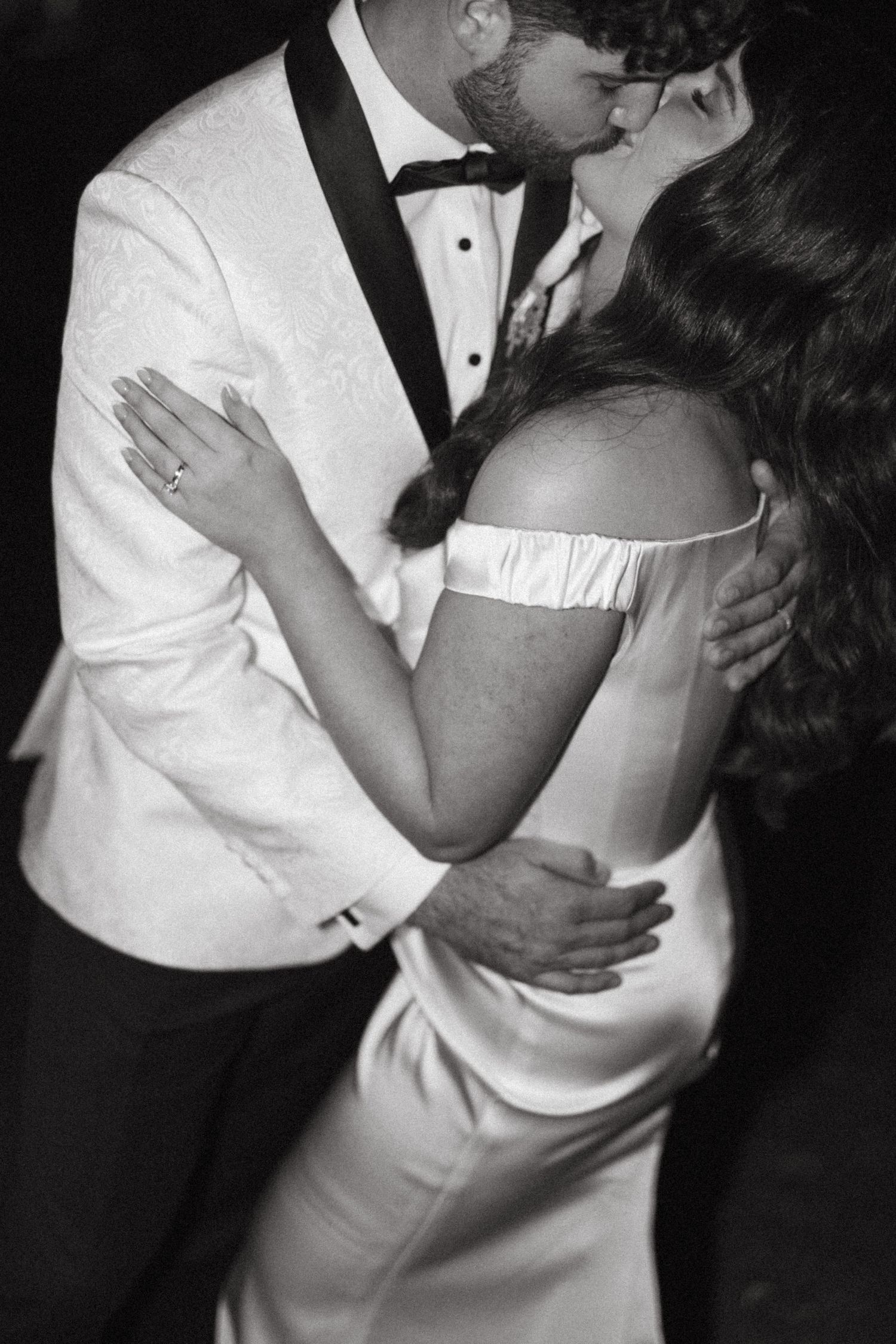A romantic black and white wedding photo showing a couple in formal attire sharing an intimate kiss.