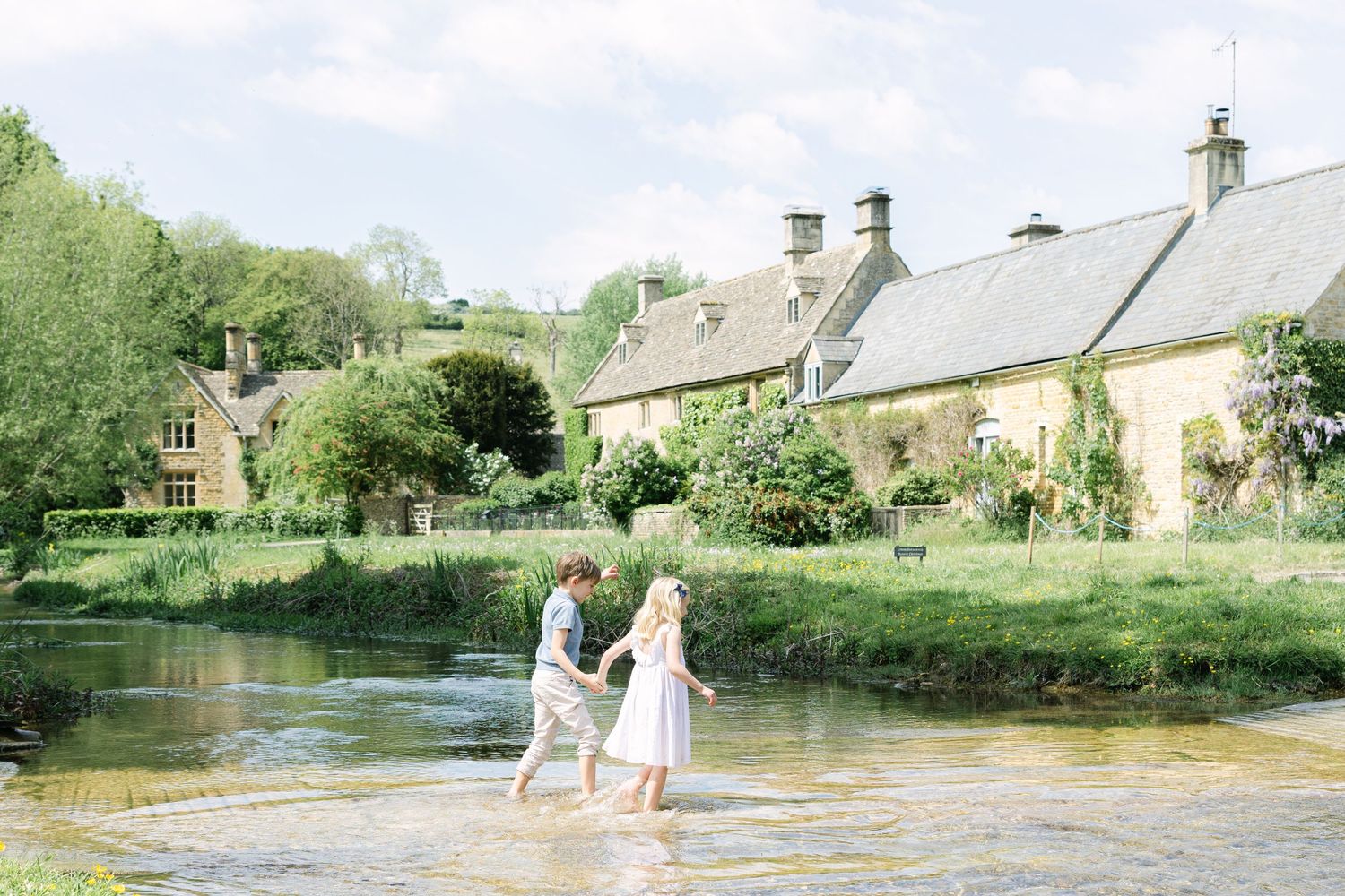 Boy and girl holding hands and walking through the river during family photo session in the cotswolds