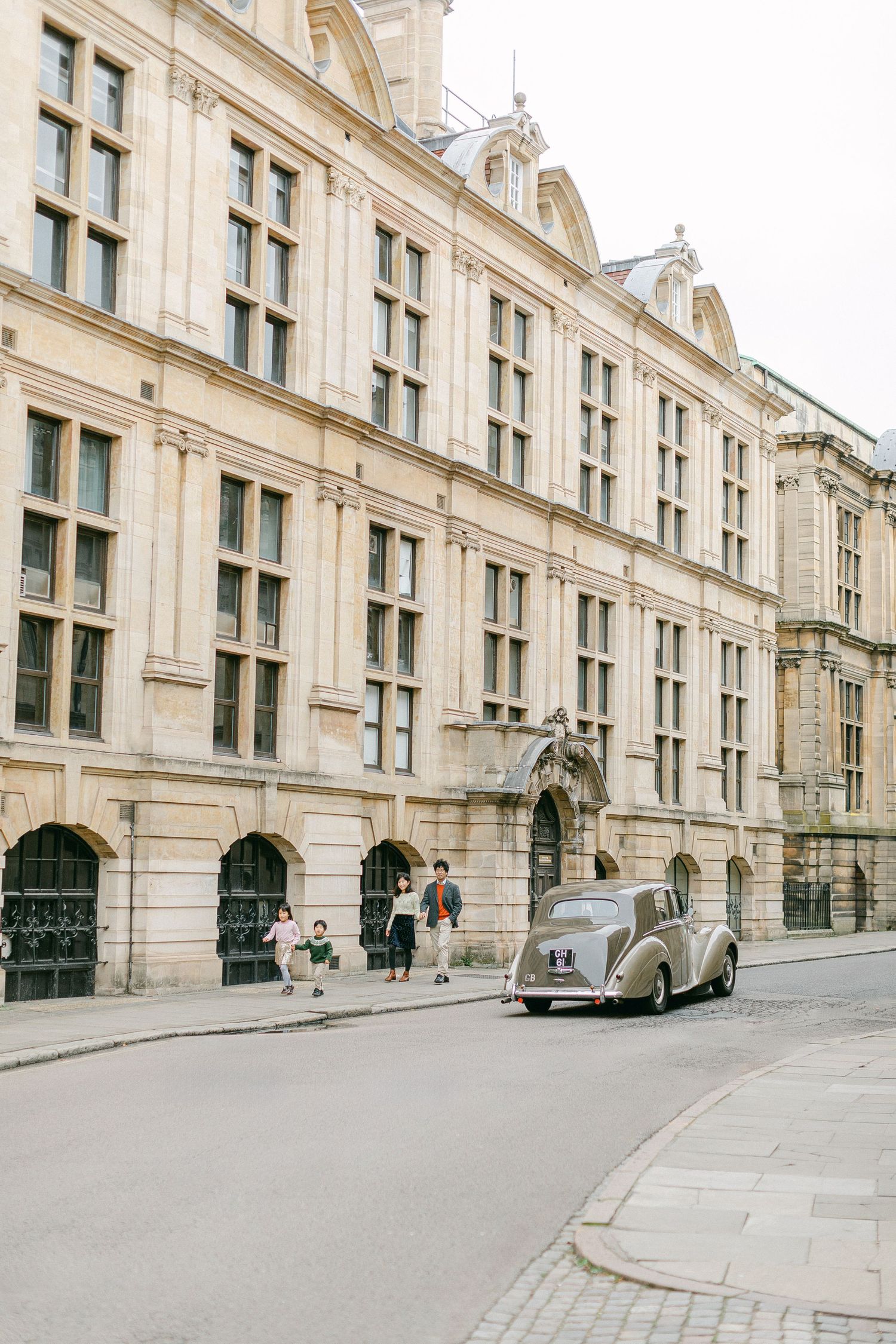 Family walking down the street in Cambridge during their family portraits while an old-style car drives by