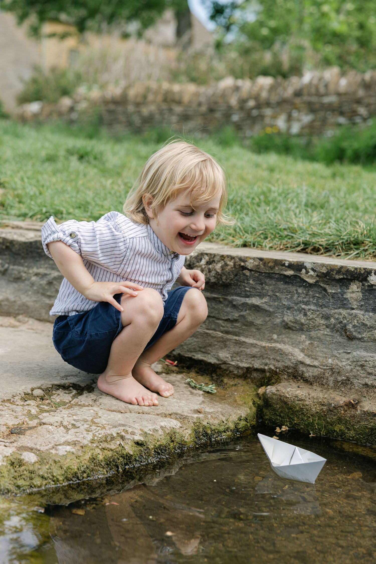Boy playing with paper boat during family photo session in the cotswolds