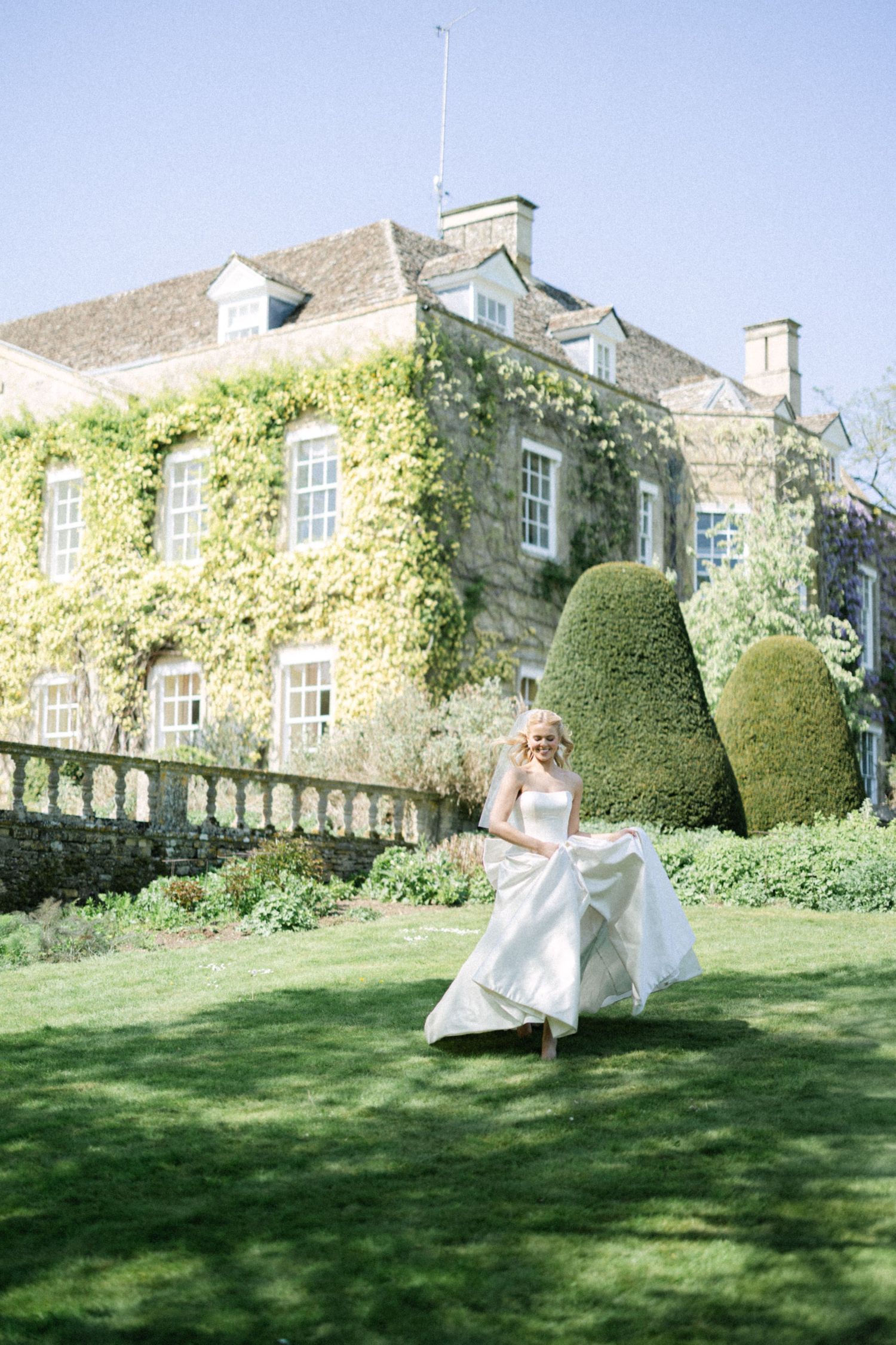 Bride running in the garden with Cornwell manor in the background