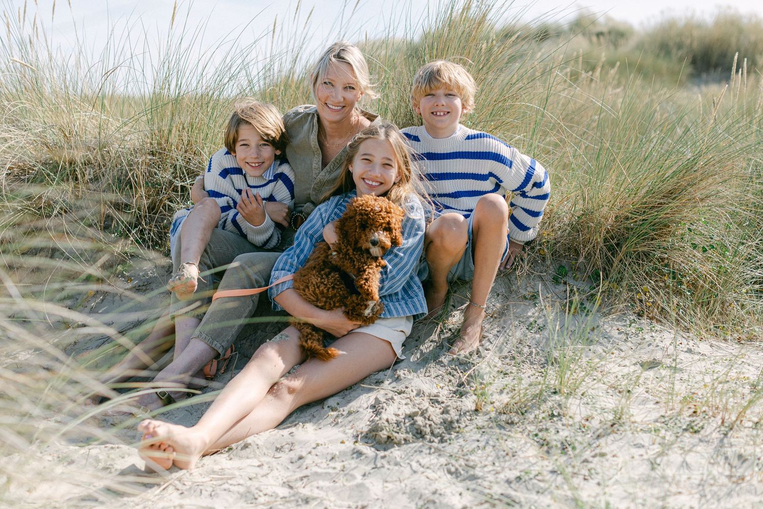 Family of 4 with their dog sitting in the dunes in West Wittering during a natural family photo session at the beach.
