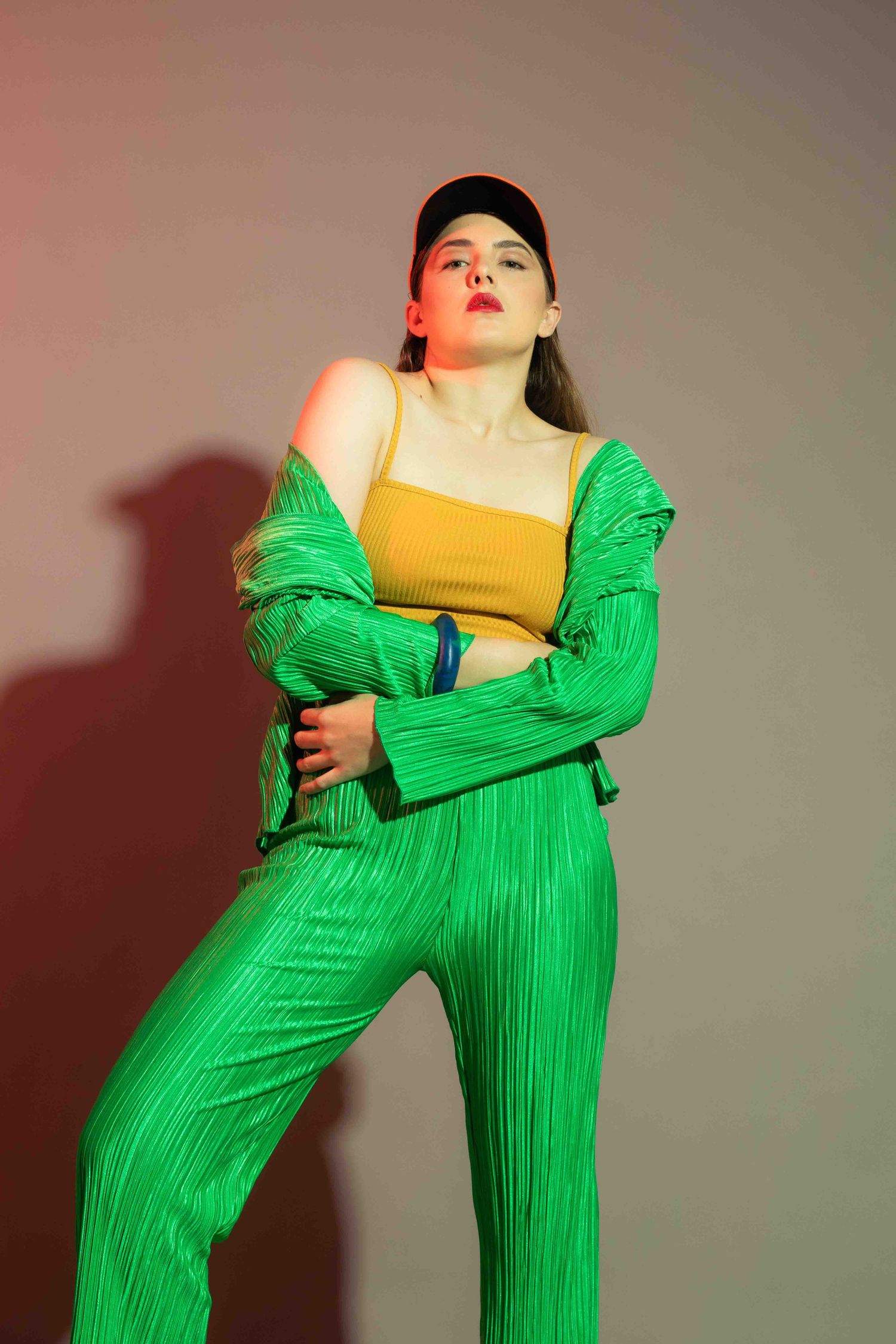 Fashion portrait in bright green pleated outfit with yellow top and baseball cap.
