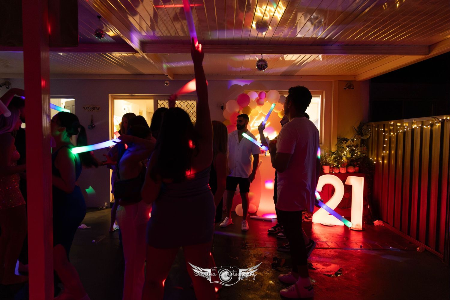 Silhouettes of party attendees dancing under red and blue lighting next to illuminated numbers.
