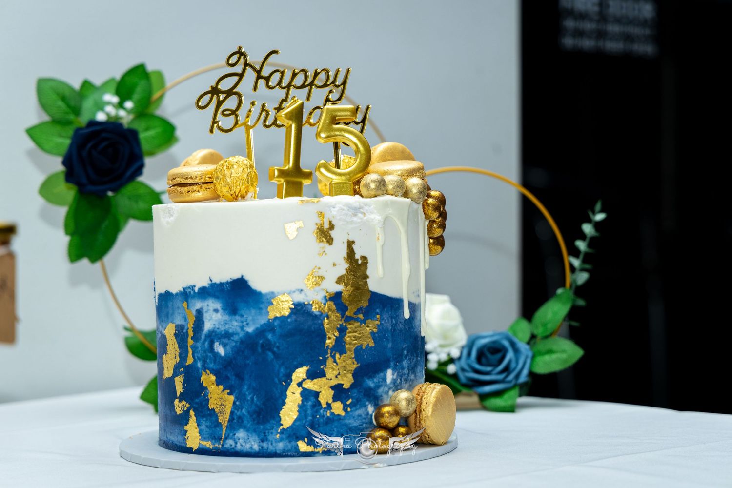 Elegant birthday cake with blue and gold marble design and 'Happy Birthday' topper on white tablecloth.