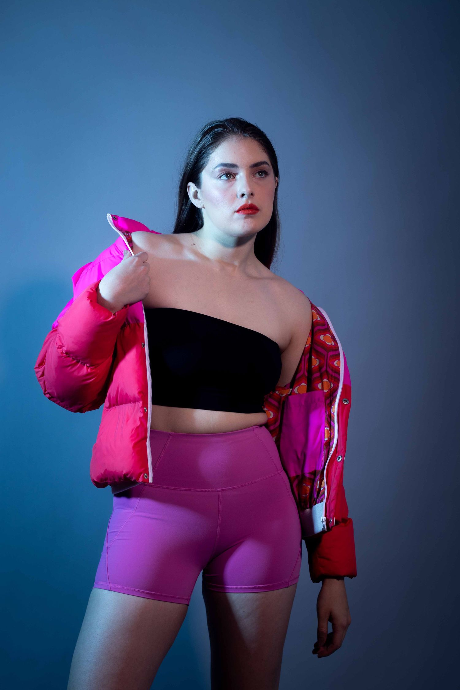 Athletic wear portrait with pink puffer jacket and shorts against blue gradient background.