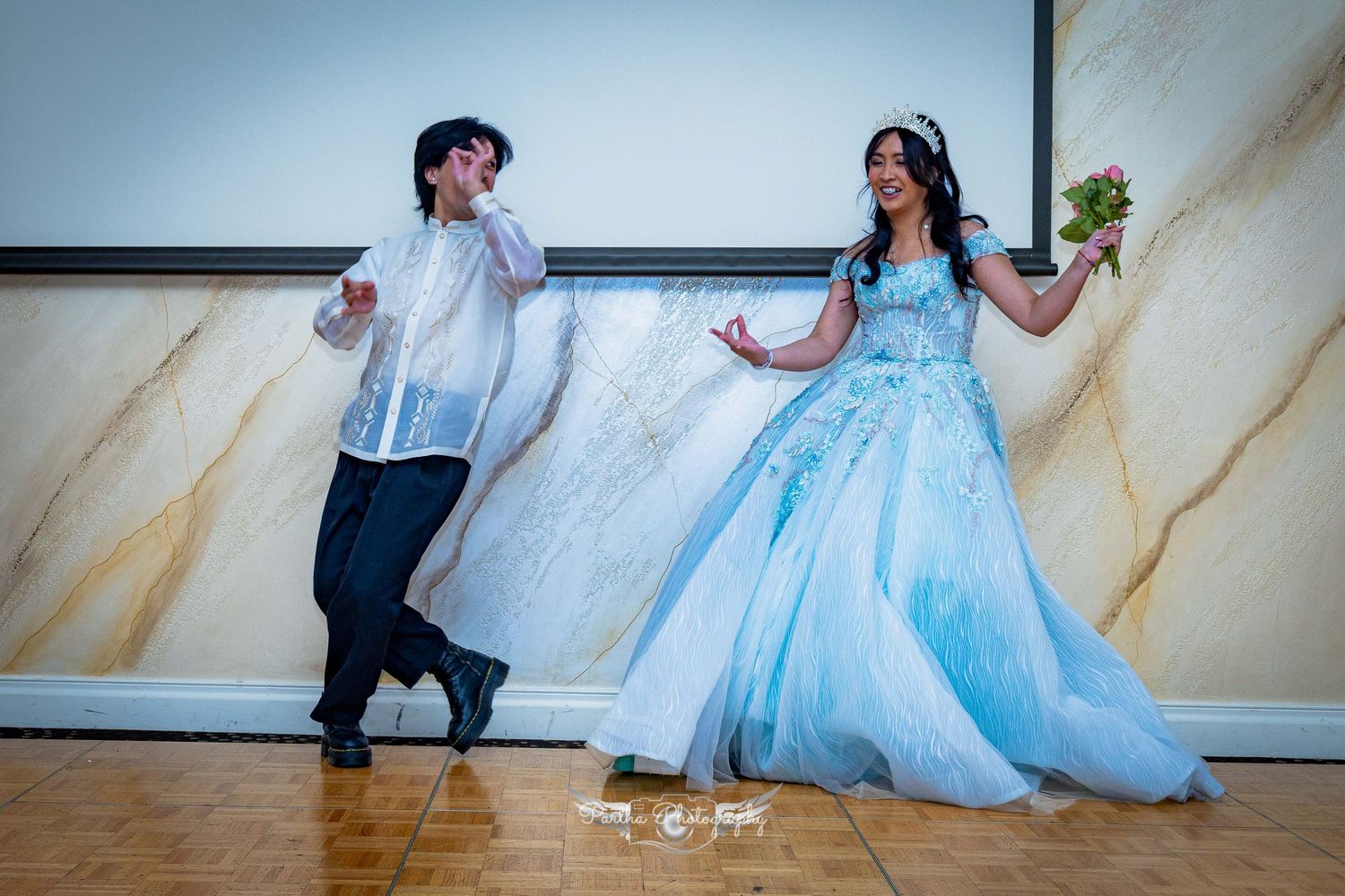 Two people having fun while dancing in formal attire against a marble-patterned wall.