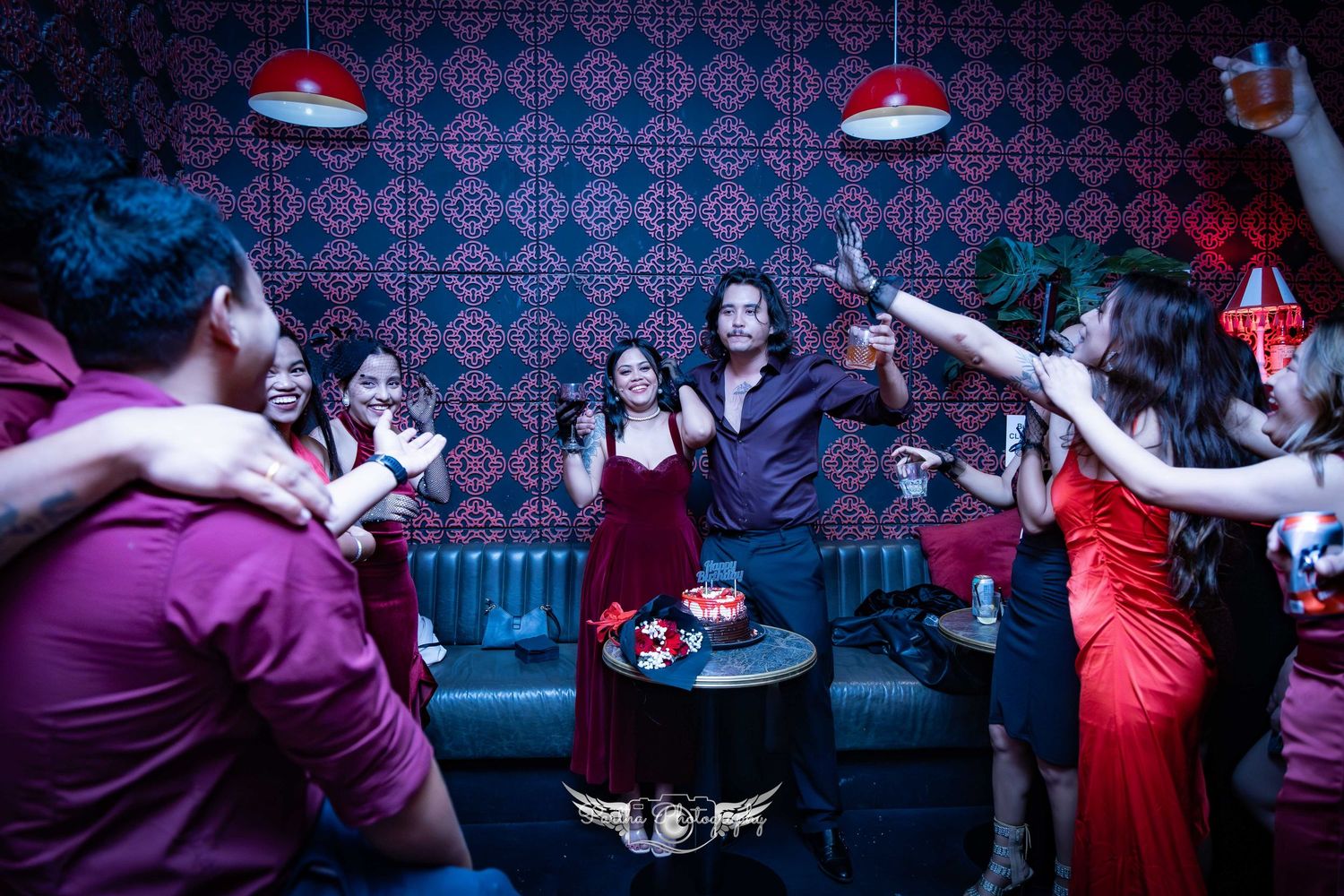 People dancing and celebrating at a nightclub party with vintage-style decor and red lighting.