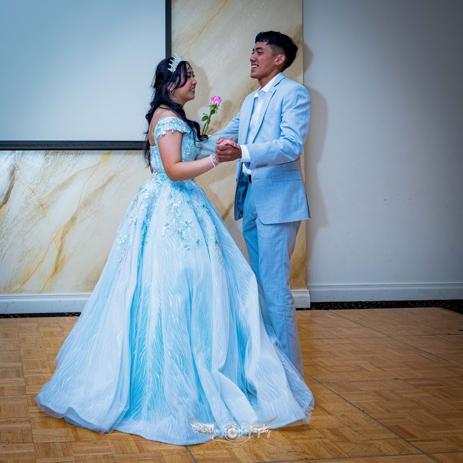 A couple dances together, with the woman wearing a flowing light blue ballgown.