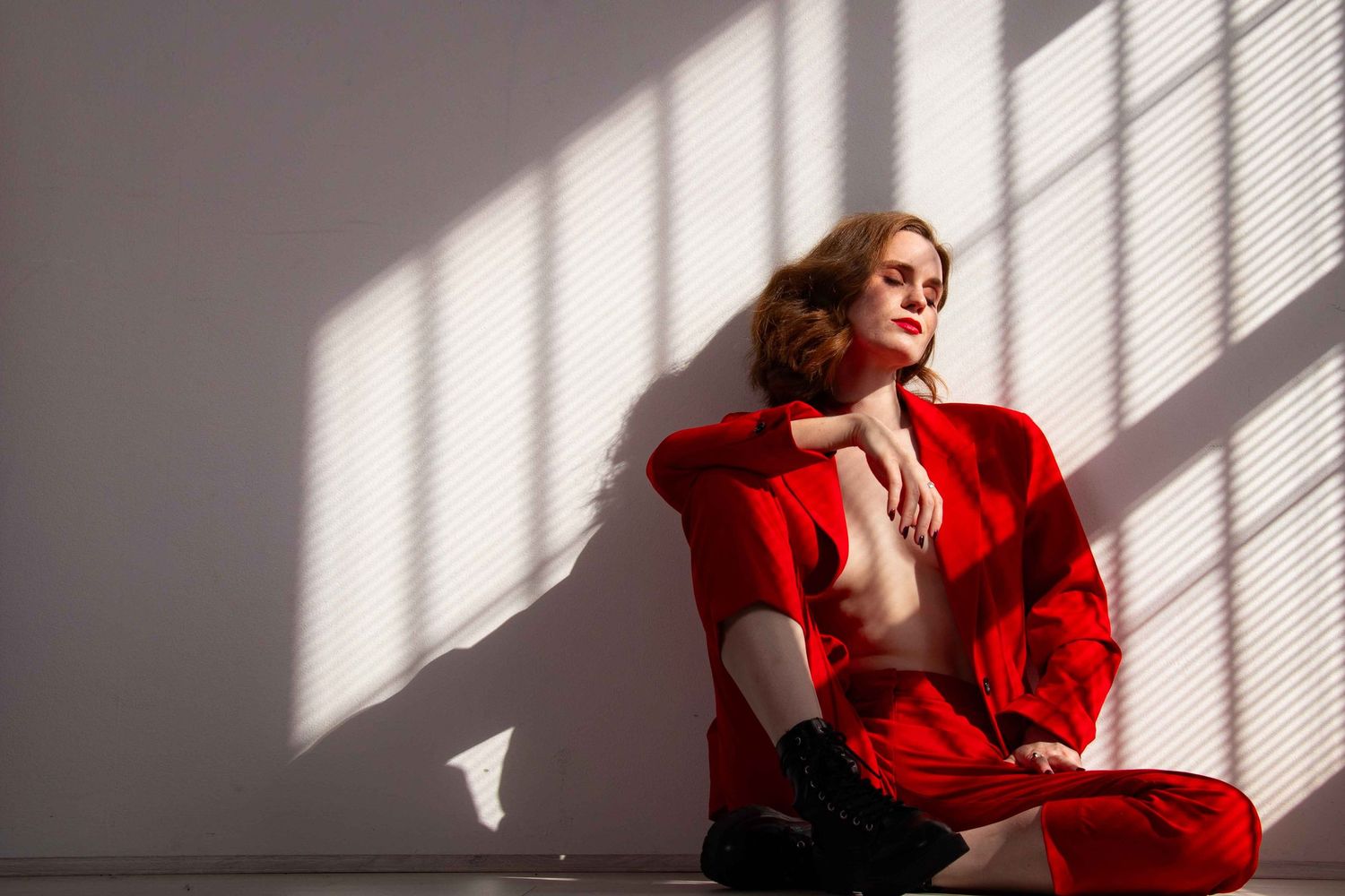 Fashion portrait in red jacket with dramatic window light casting shadows.