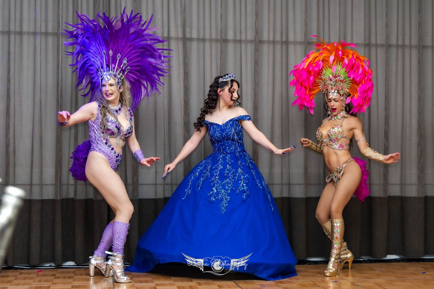 Dancers in carnival costumes and blue ballgown performing choreographed routine on stage.