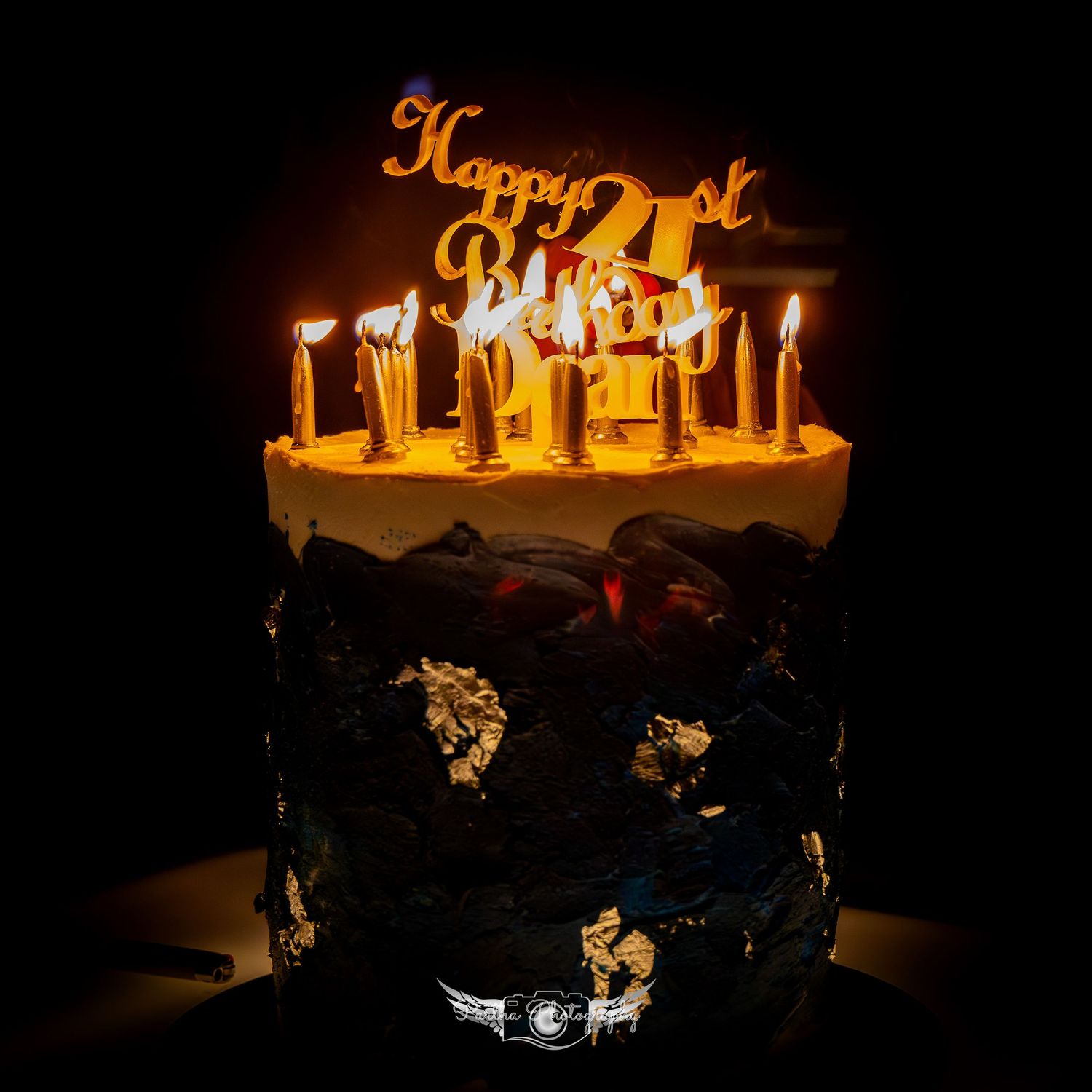 Birthday cake with glowing candles and golden '21st' topper against black background.