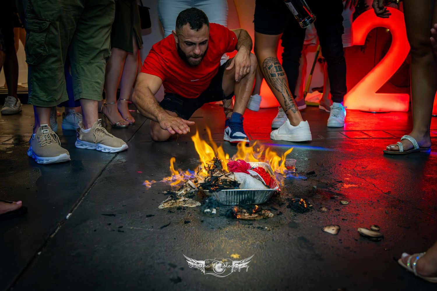 A small fire burns on the floor surrounded by people's feet at a celebration.
