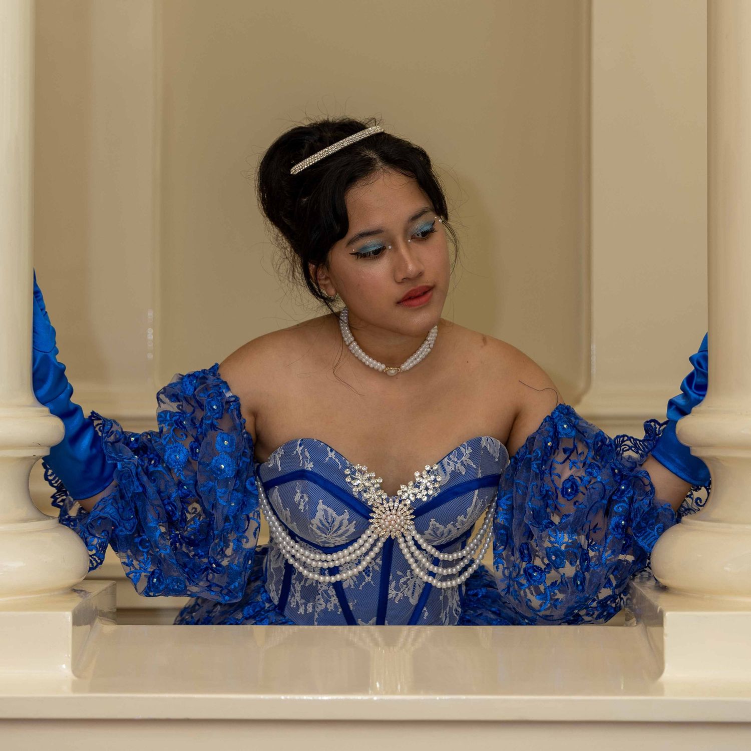 Elegant portrait in blue lace corset dress with crystal details against beige backdrop.