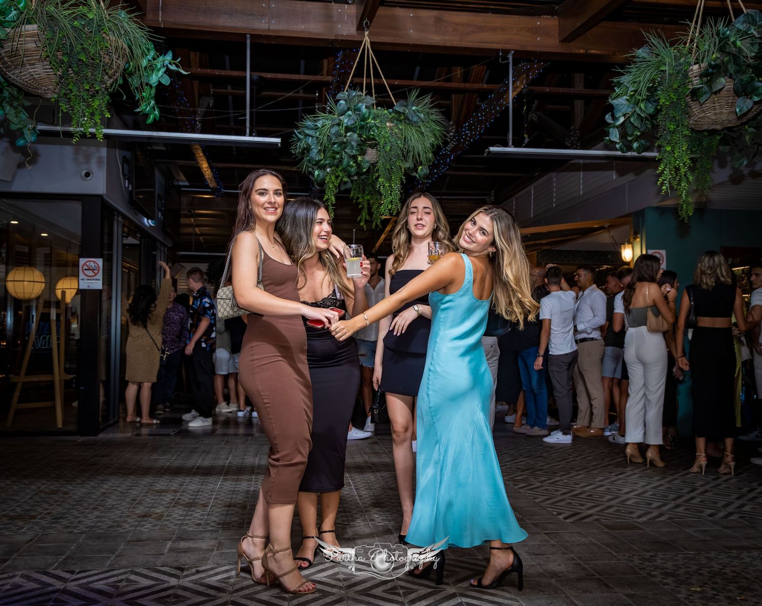 Guests dancing under decorative hanging plants at indoor celebration.