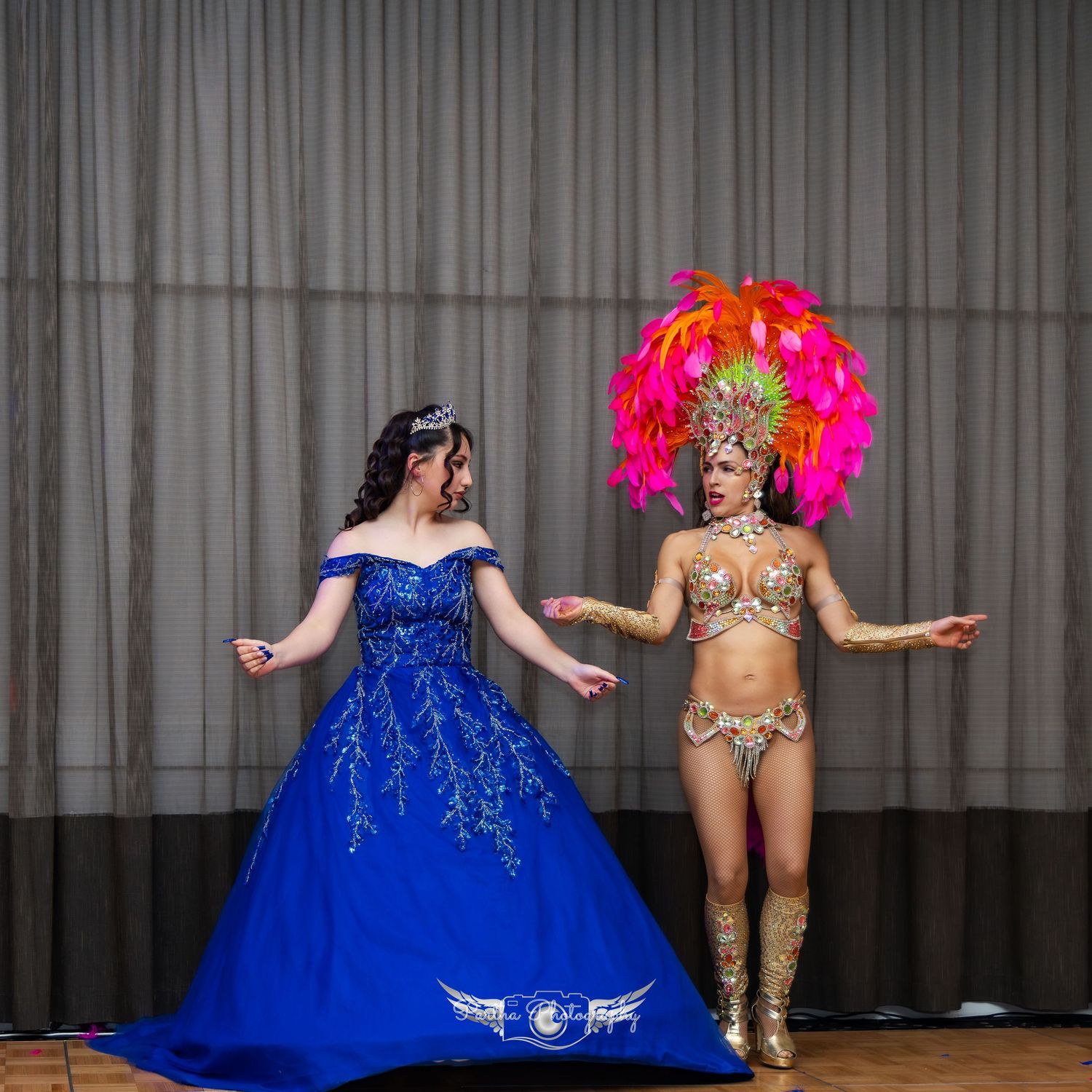 Contrasting performers in blue ballgown and colorful carnival costume pose on stage.