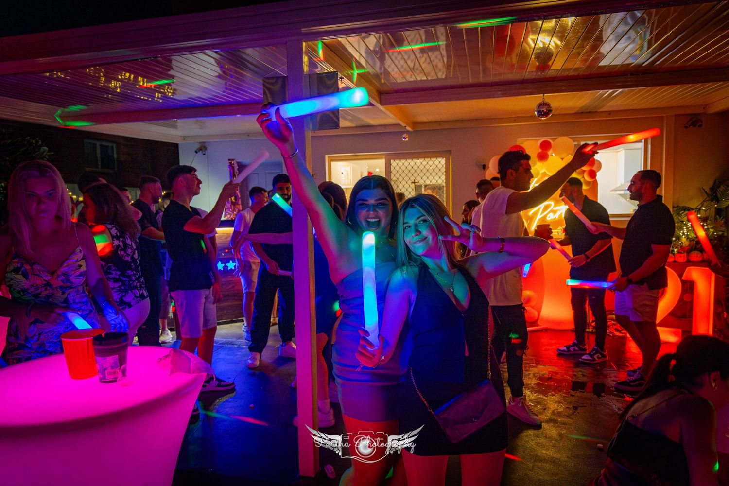 Partygoers dance under colorful lighting with glowing blue LED accessories.