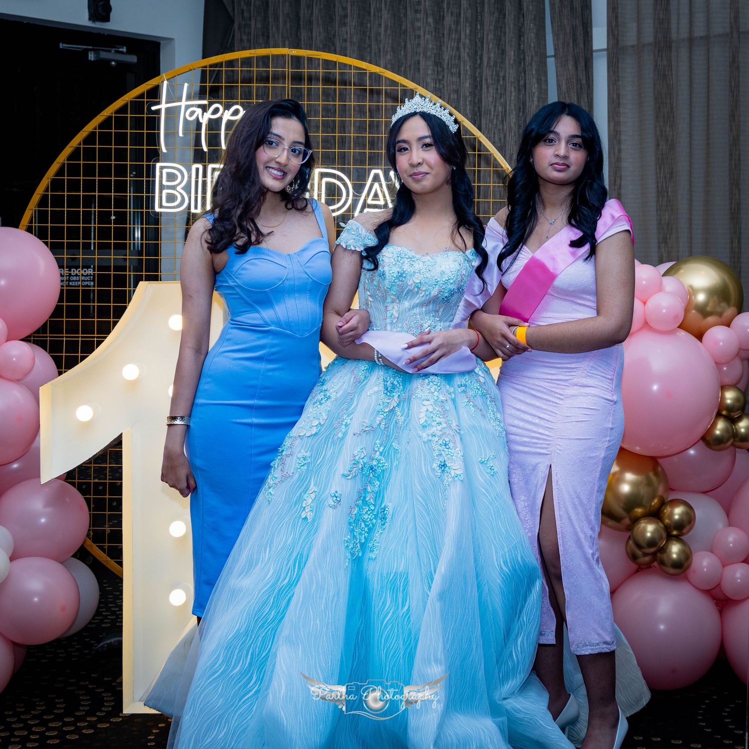 Birthday celebration setup with pink and gold balloon arch and decorative lighting.
