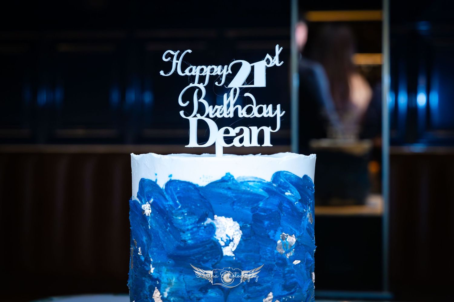 Blue birthday cake with a '21st Birthday' topper against dark background.