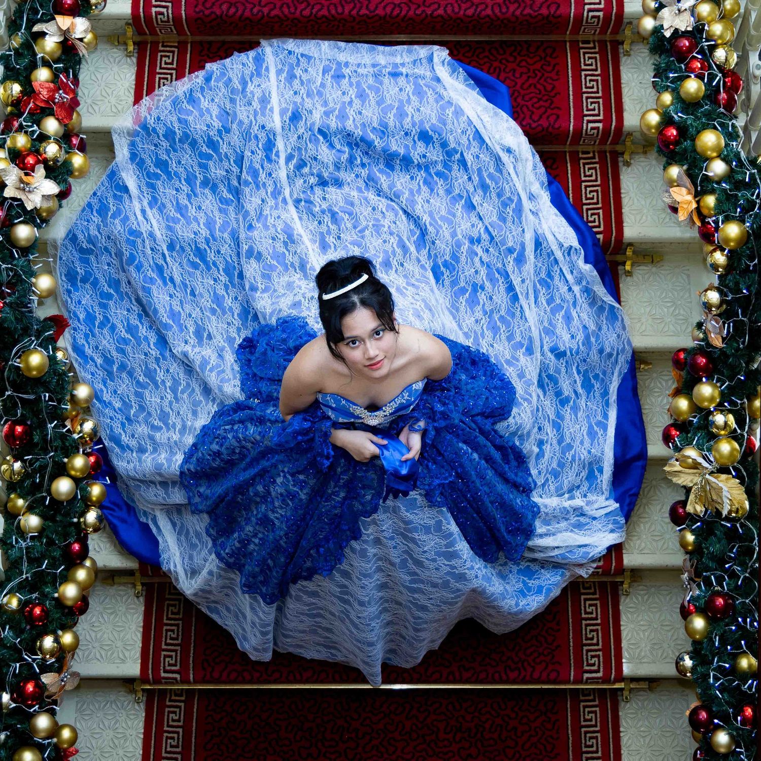 Person in a flowing blue ballgown dress lying gracefully on decorative carpet.