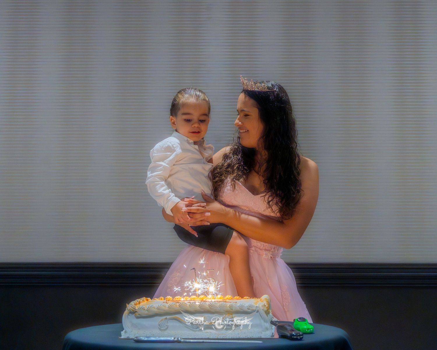 A woman in a pink dress celebrating with a small child next to a decorated cake.