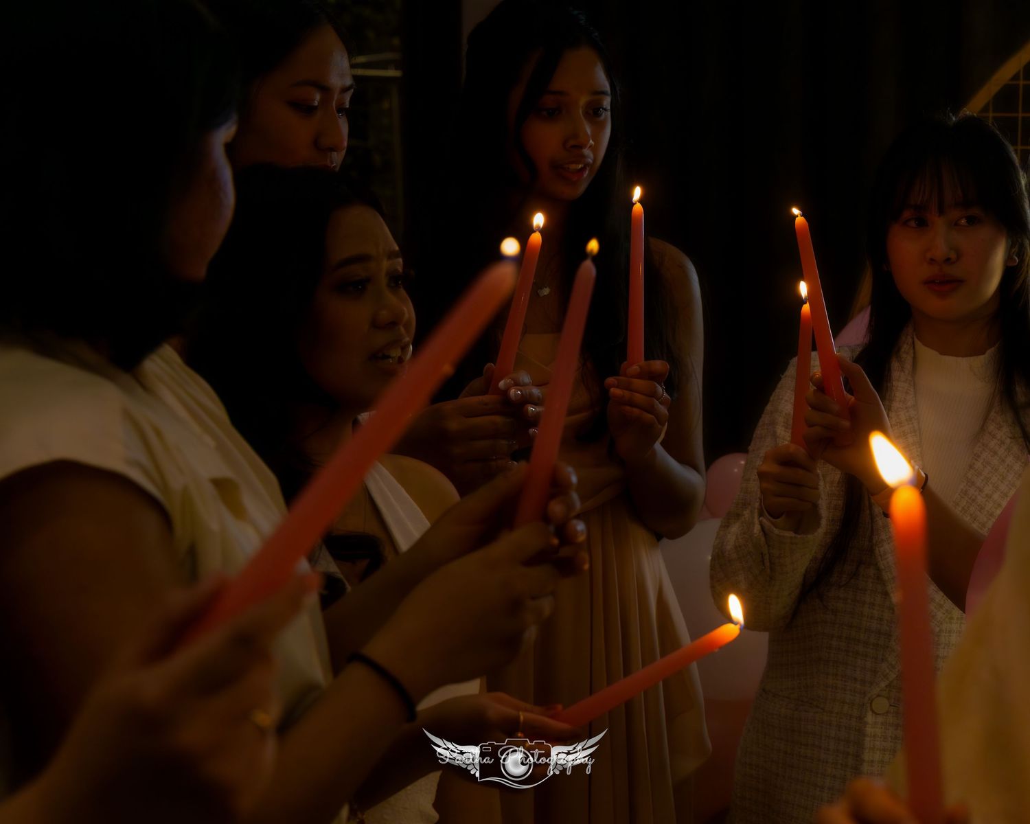 People hold lit candles in a dimly lit room during a ceremonial gathering.