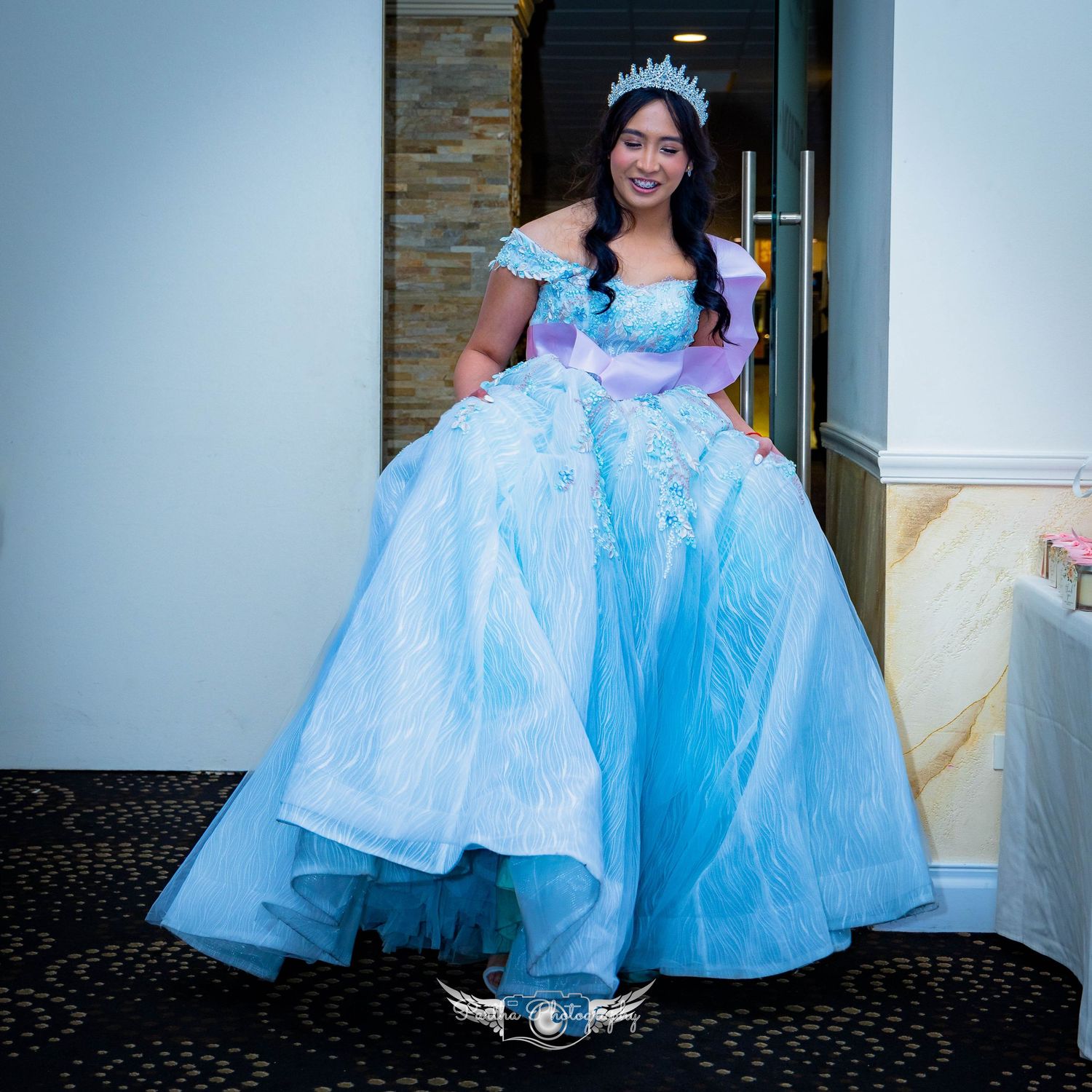 Person wearing an elegant light blue ball gown and tiara standing in a doorway.