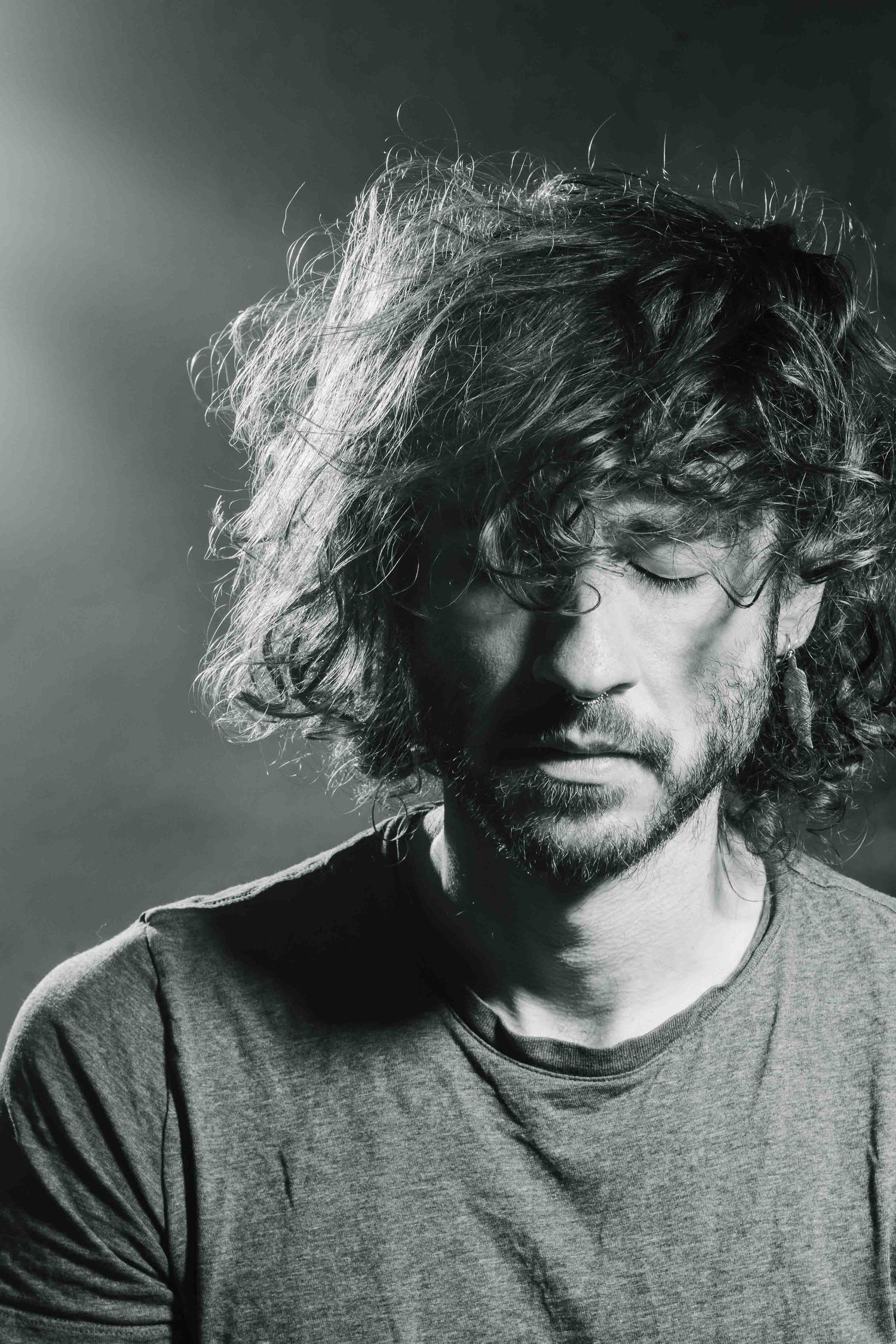 Black and white portrait showcasing curly hair and moody lighting against dark background.