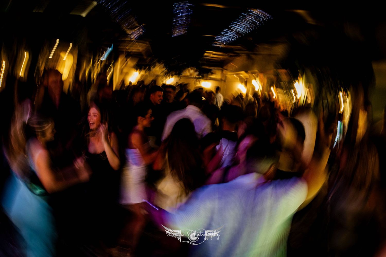 Motion blurred crowd dancing at a nightclub with colorful lights creating an energetic atmosphere.