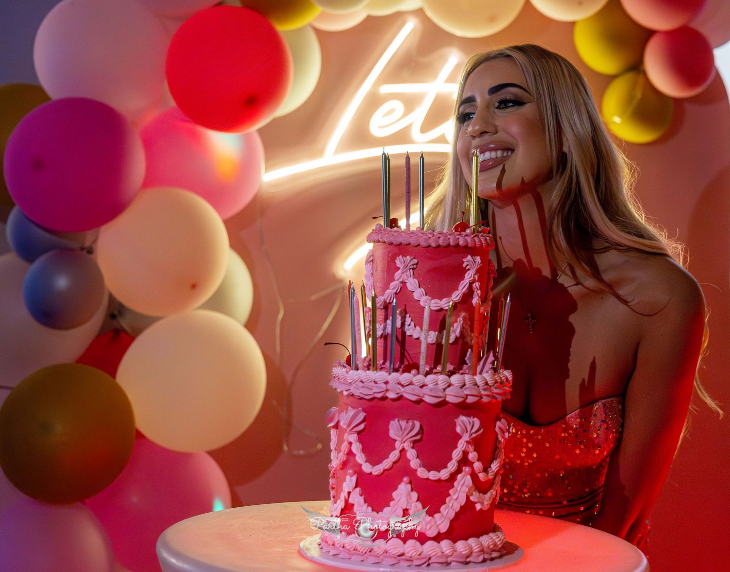Person in red dress smiling with lit birthday cake and balloon decorations.