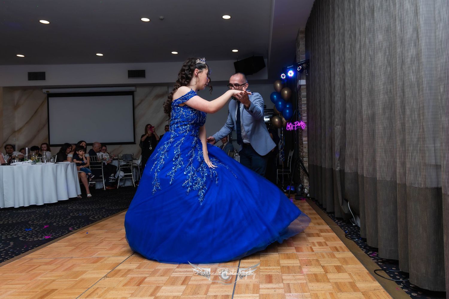 A couple slow dancing on a wooden dance floor while guests watch in the background.