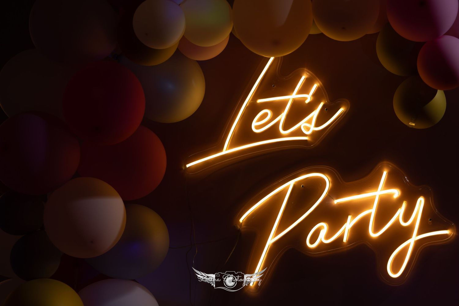 Neon 'Let's Party' sign glowing against dark background with colorful balloons.