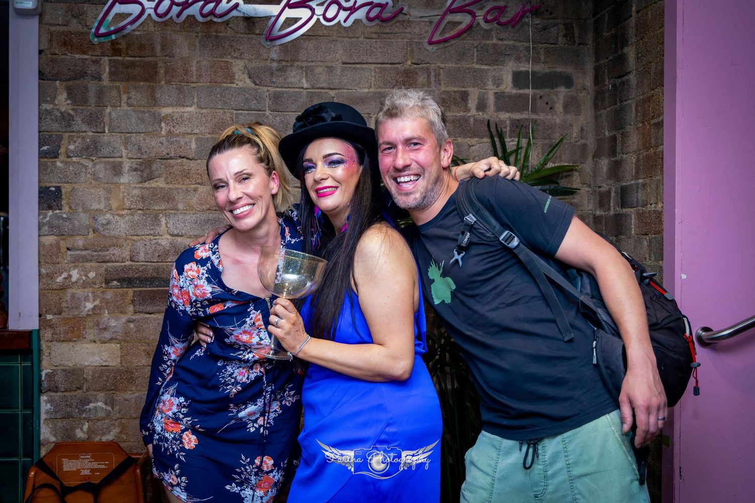 Party guests posing together at a celebration with brick walls and purple lighting.