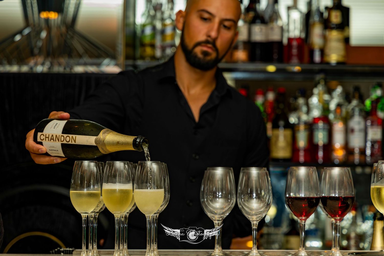Bar counter with lined up glasses and bartender preparing drinks.