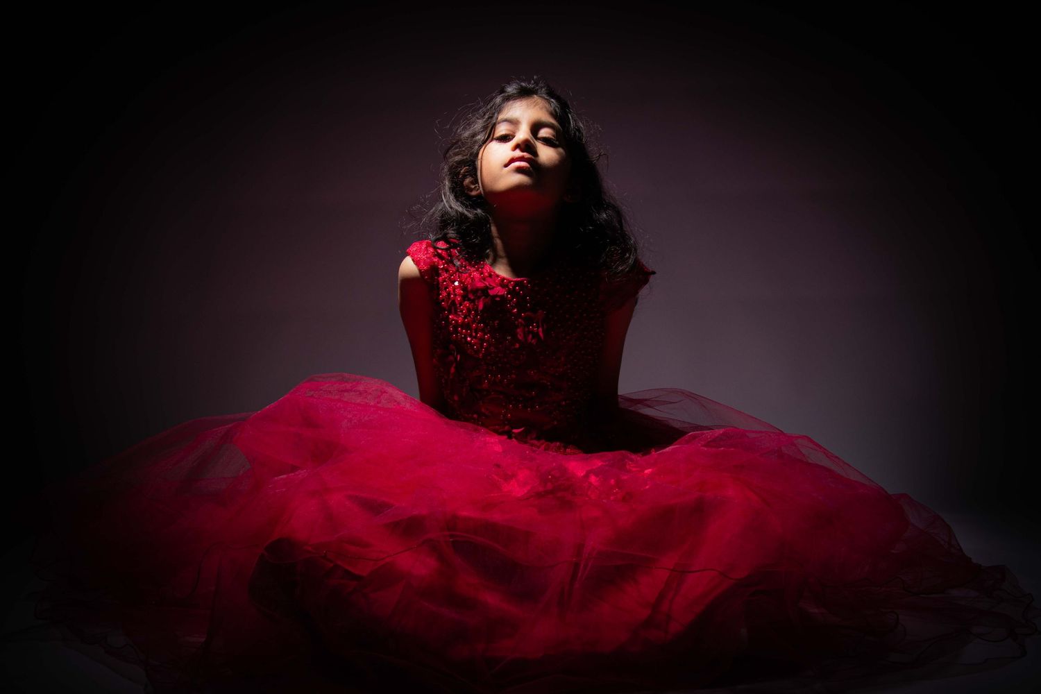 Dramatic portrait of figure in red gown against dark background with moody lighting.