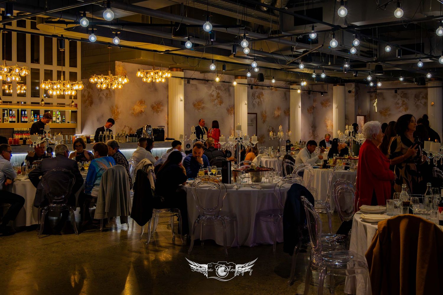 An elegant reception venue with chandeliers and decorated tables filled with guests enjoying the evening.