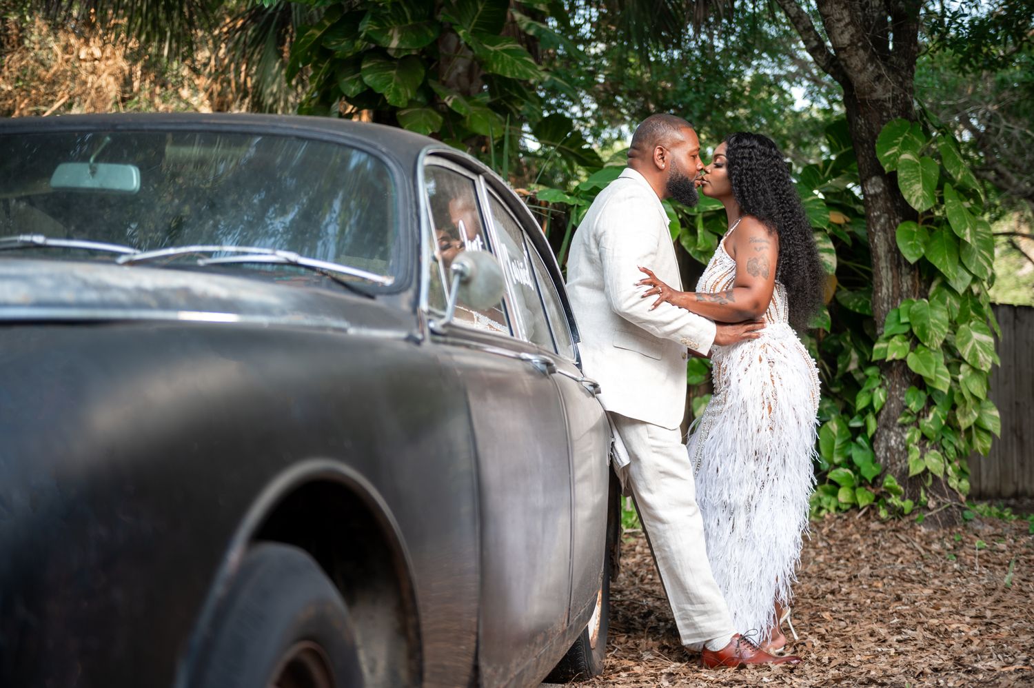 A groom kisses his bride next to a classic car captured by luxury wedding photographers in Palm Beach during luxury wedding portraits time