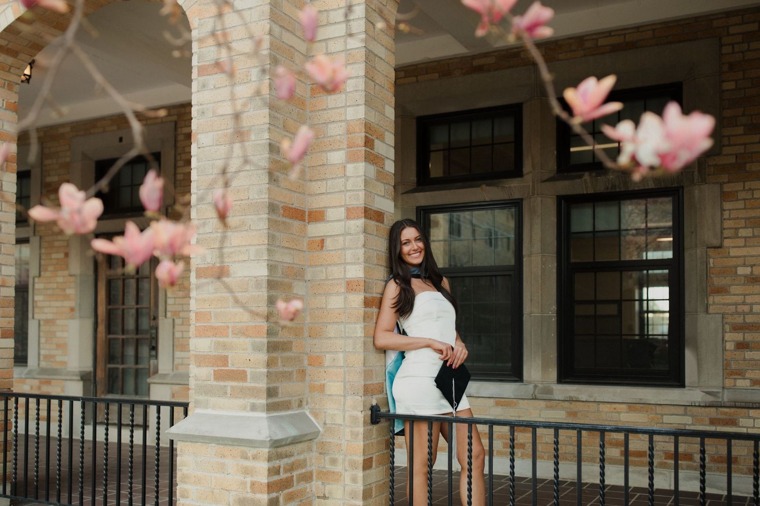 Pink floral petals float in the breeze at a brick building entrance with stone columns and black railings.