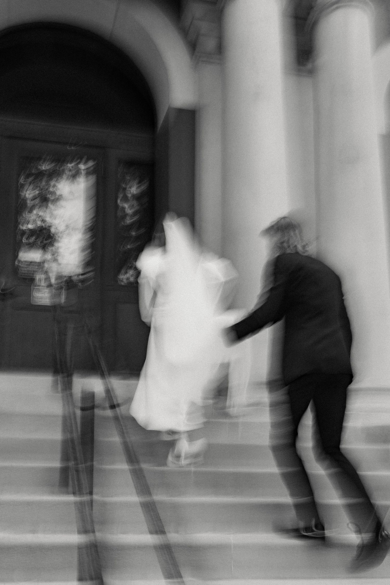 Artistic motion blur black and white photo of couple ascending grand entrance stairs.